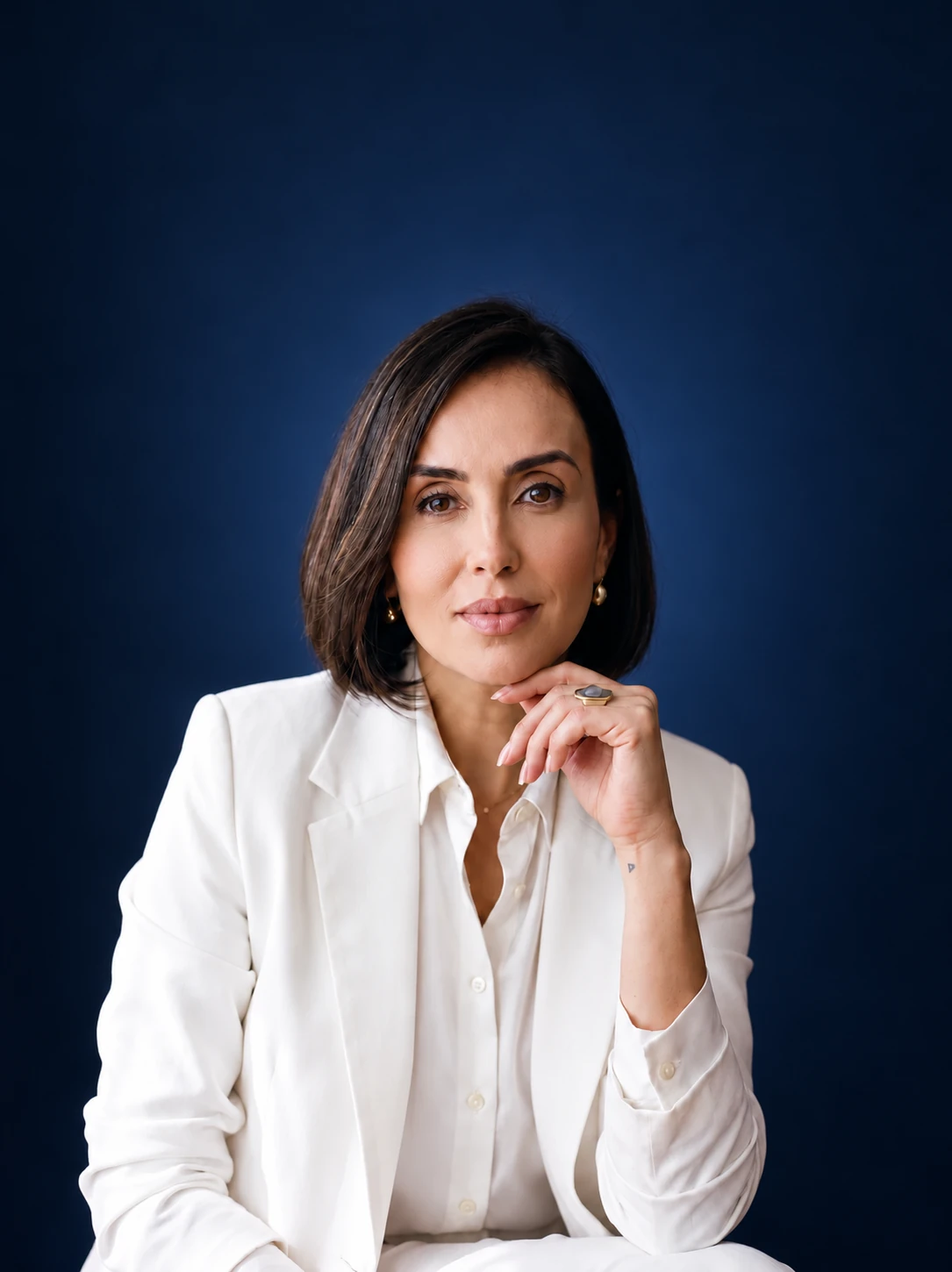 Tata de Amorim com blazer branco, em retrato com fundo azul profundo